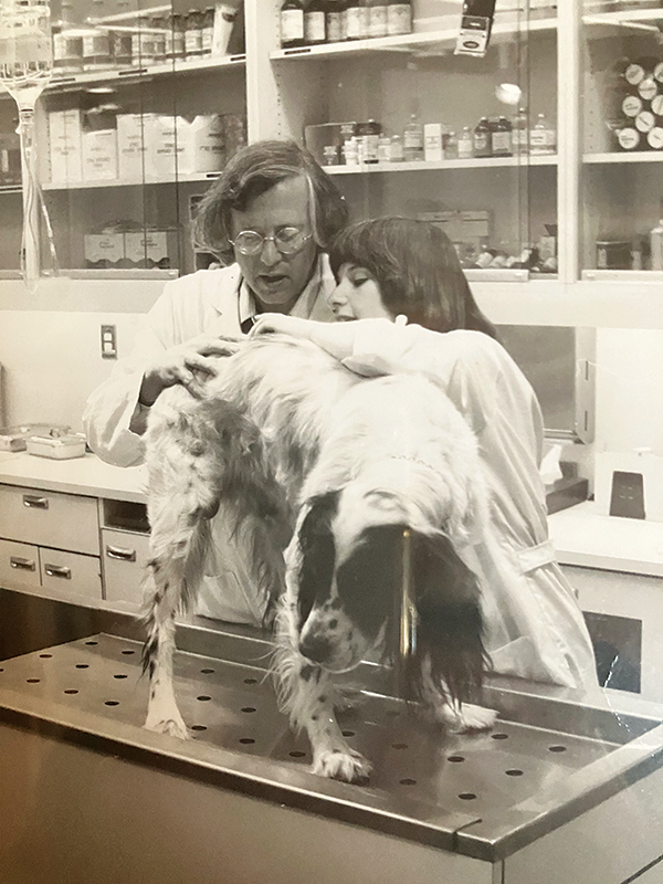 A B&W photo of Nancy Ehrlich as a young vet student assisting with a dog.