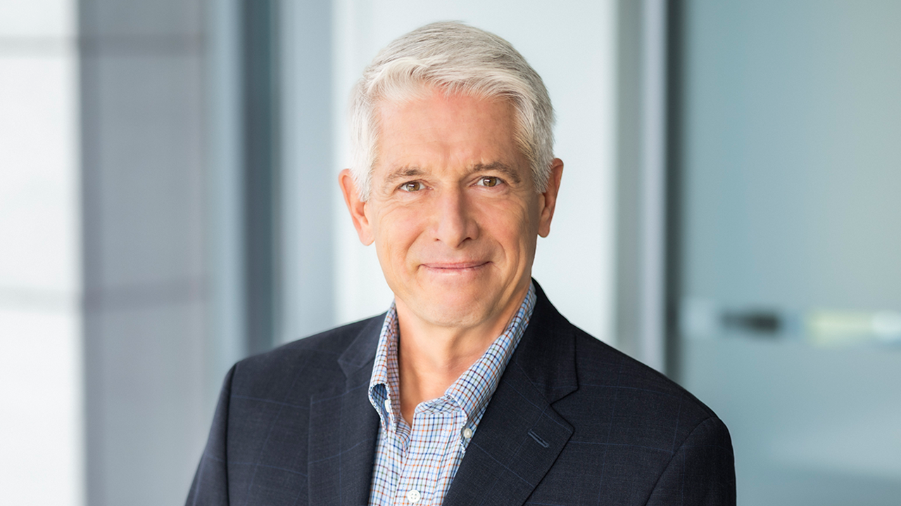 Professional headshot—mature man with gray hair, navy blazer and slight smile in office