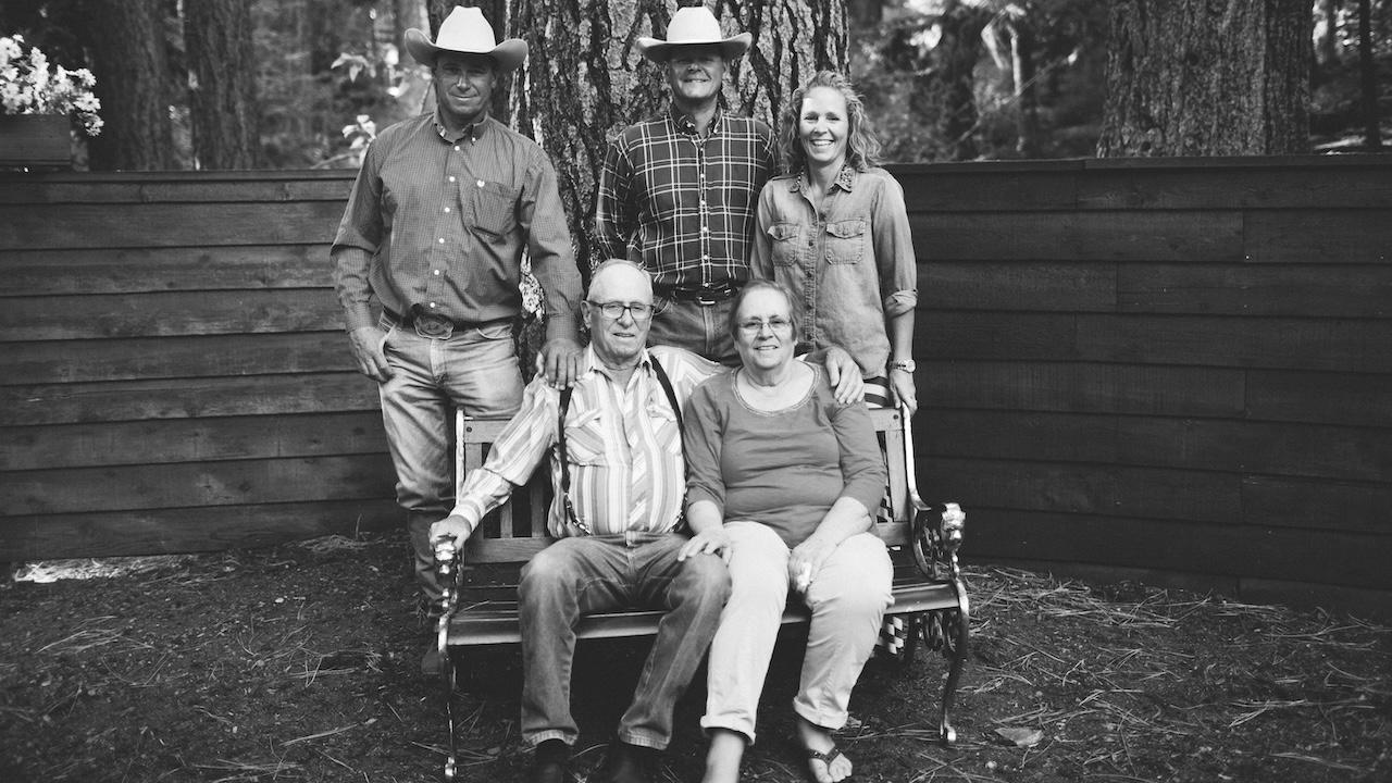 Black-and-white outdoor group portrait: two seated elders, three adults standing, smiling