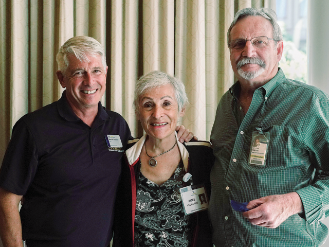 Three smiling older adults wearing name tags at an indoor social gathering